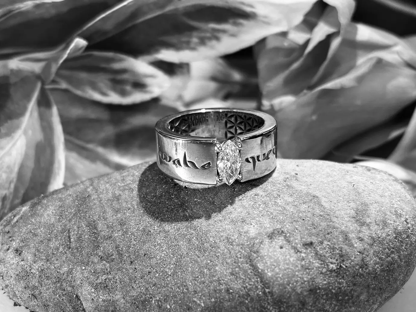 Black and white photograph of a silver ring on a stone, with engraved script